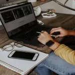 an image of someone working at their desk, with a laptop, notepad and iPhone.
